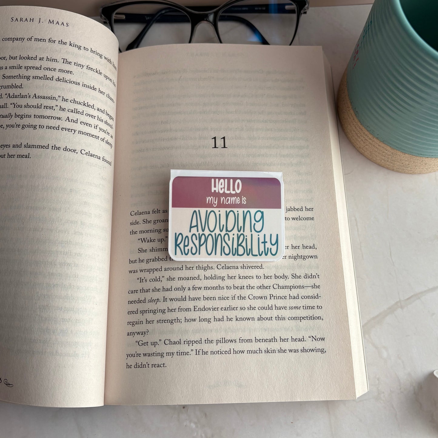Open book with a bookmark on a desk next to a mug and glasses