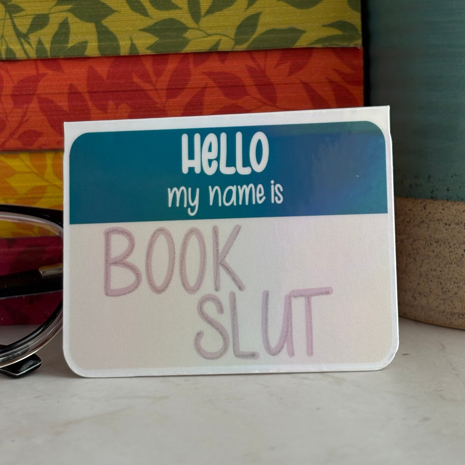 Magnetic bookmark reading, 'Hello my name is Book Slut' on a textured surface.