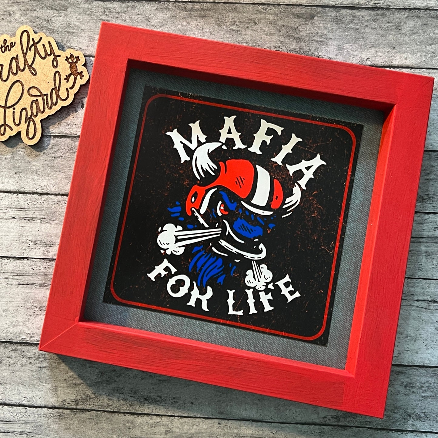 Square red frame with no glass. Denim blue paper background with illustration of an angry blue Buffalo head wearing a red and white football helmet. Says “Mafia for life”.