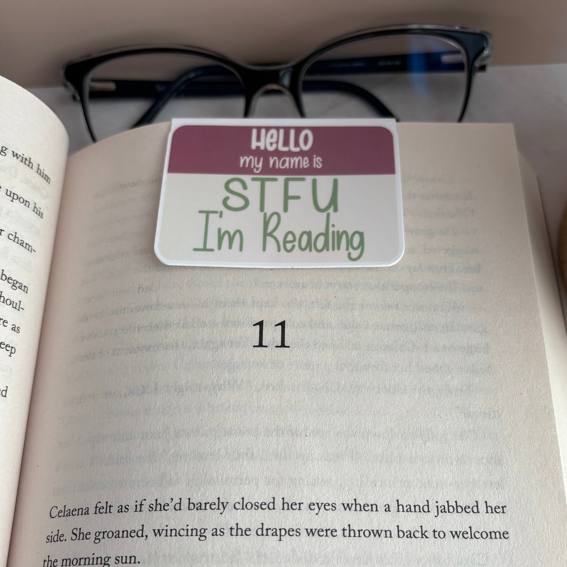 Book with a name tag style magnetic bookmark reading 'Hello my name is STFU I'm Reading' on a shelf.